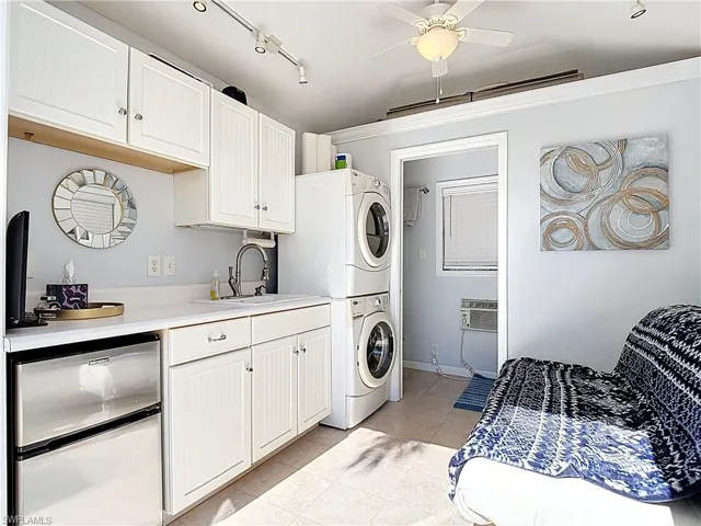 Washroom featuring stacked washer and clothes dryer, light tile patterned floors, ceiling fan, a wall mounted AC, and ornamental molding