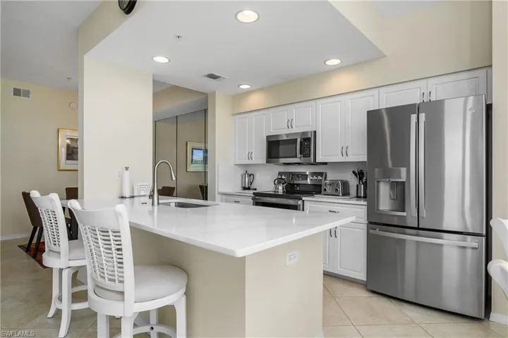 Kitchen with light tile patterned flooring, a sink, stainless steel appliances, a kitchen bar, and visible vents