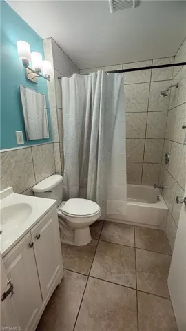 Full bath with shower / bath combo, vanity, tile walls, and light tile patterned flooring