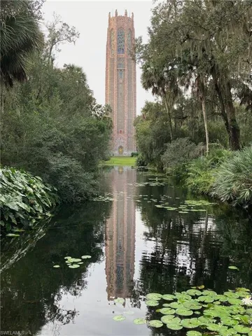 Tall historic tower with intricate stonework and colorful window details, situated among mature trees