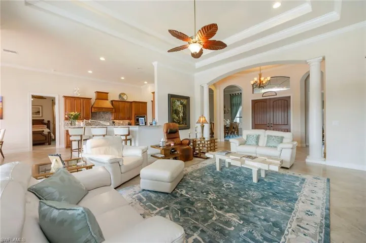 Living room with arched walkways, a tray ceiling, a chandelier, crown molding, and recessed lighting