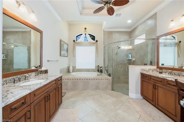 Bathroom featuring a stall shower, a bath, ornamental molding, two vanities, and ceiling fan