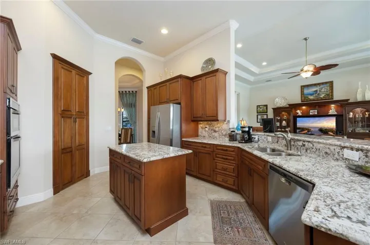 Kitchen with arched walkways, stainless steel appliances, a kitchen island, brown cabinetry, and ornamental molding