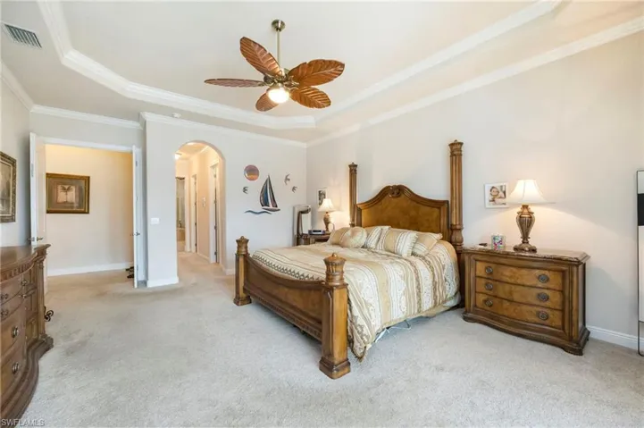 Carpeted bedroom with crown molding, arched walkways, ceiling fan, and a tray ceiling