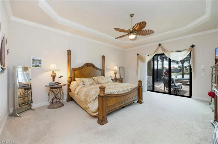 Bedroom with access to exterior, light colored carpet, ceiling fan, ornamental molding, and a tray ceiling