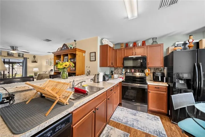 Kitchen with black appliances, light countertops, open floor plan, and wood finish cabinetry