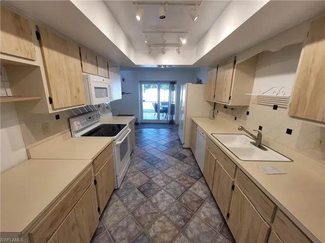 Kitchen with light brown cabinetry, decorative backsplash, white appliances, open shelves, and light countertops