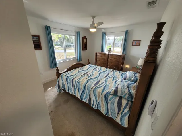 Carpeted bedroom with multiple windows, a ceiling fan, and a textured wall