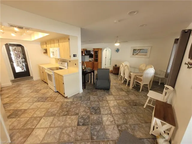 Kitchen featuring arched walkways, white appliances, light countertops, and light brown cabinetry