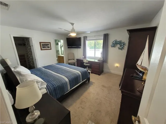 Bedroom with light colored carpet, a walk in closet, ceiling fan, and connected bathroom