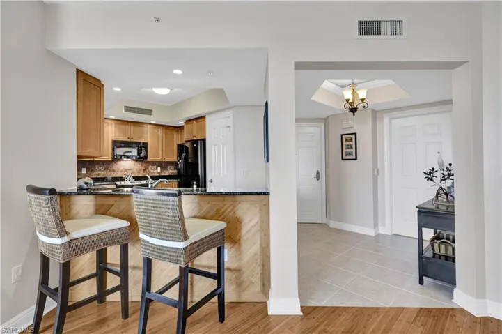 Kitchen featuring pantry, black appliances, granite  breakfast bar, and decorative backsplash