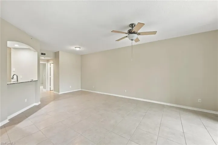 Tile flooring, neutral wall tones, ceiling fan with light fixture, arched pass-through, and a bar-height counter with a pull-down faucet