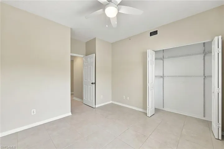 Light-toned tile flooring, neutral wall color, ceiling fan with integrated lighting, bi-fold closet doors, and adjustable closet shelving system