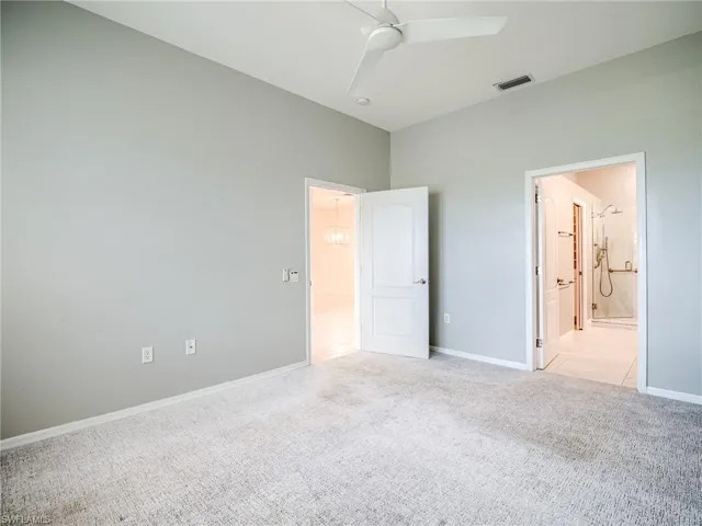 Unfurnished bedroom featuring light colored carpet, ensuite bathroom, and ceiling fan