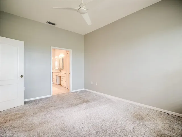 Unfurnished bedroom featuring ceiling fan, connected bathroom, and light colored carpet