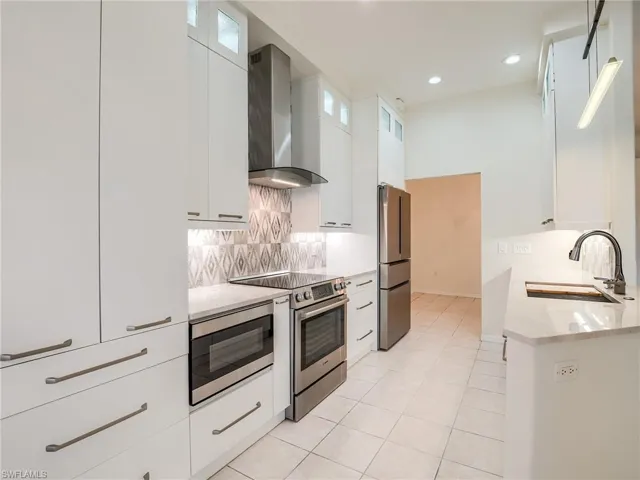 Kitchen featuring appliances with stainless steel finishes, backsplash, sink, wall chimney range hood, and white cabinets
