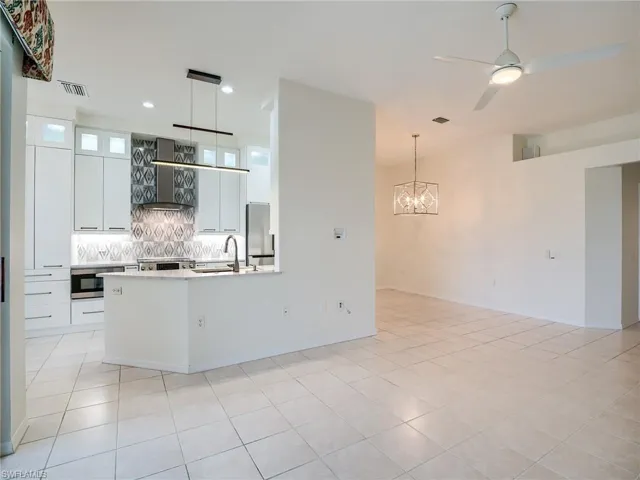 Kitchen featuring wall chimney range hood, stainless steel refrigerator, hanging light fixtures, and white cabinetry