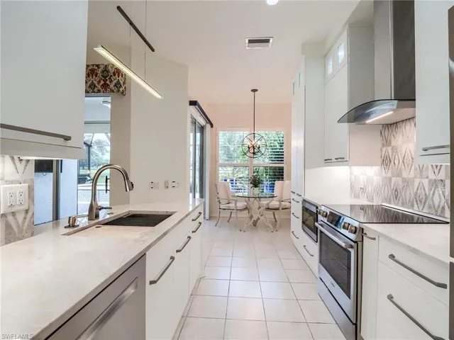 Kitchen with wall chimney range hood, white cabinets, appliances with stainless steel finishes, and a healthy amount of sunlight
