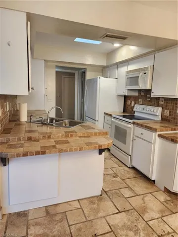 Kitchen featuring decorative backsplash, stove, tile countertops, and white cabinets