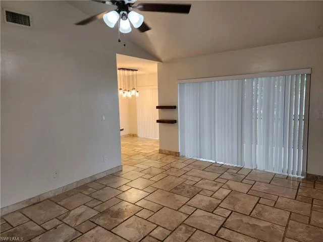 Unfurnished room with vaulted ceiling, stone tile flooring, ceiling fan, and a chandelier