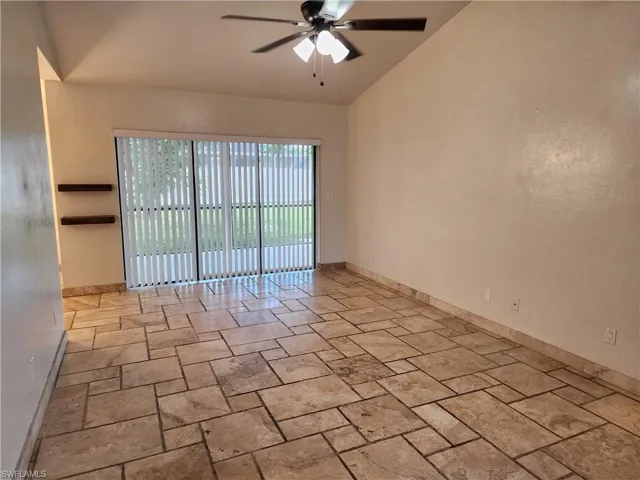 Empty room featuring a ceiling fan, vaulted ceiling, and stone tile flooring