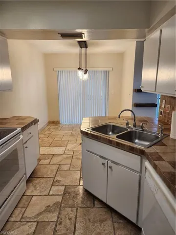 Kitchen with stove, white cabinets, dishwashing machine, hanging light fixtures, and stone tile floors