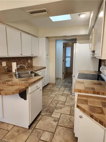 Kitchen with decorative backsplash, white cabinetry, a skylight, and stone tile flooring