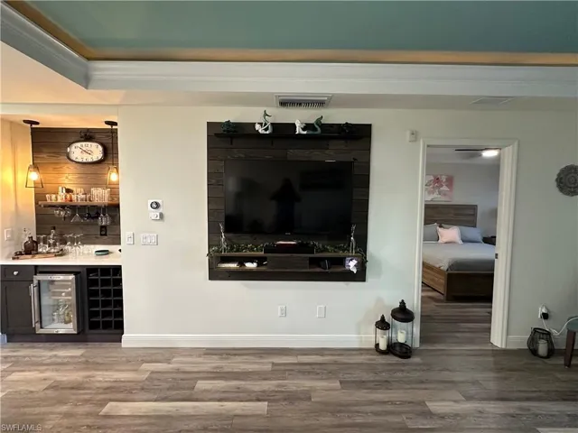 Indoor bar featuring wine cooler, crown molding, open shelves, and dark cabinetry