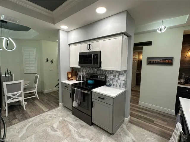 Kitchen featuring a tray ceiling, electric range, gray cabinets, white cabinetry, and crown molding