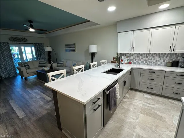 Kitchen featuring gray cabinets, a breakfast bar, open floor plan, light stone counters, and a tray ceiling