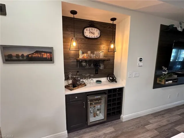 Indoor dry bar featuring wine cooler, open shelves, dark cabinets, and light stone countertops
