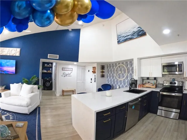 Kitchen with open floor plan, stainless steel appliances, a peninsula, white cabinets, and light stone countertops