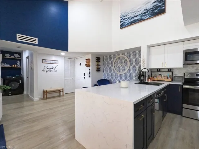 Kitchen with white cabinetry, a peninsula, a towering ceiling, dark cabinets, and appliances with stainless steel finishes