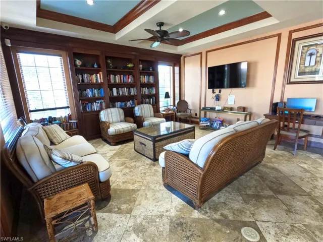 Living area featuring a raised ceiling, ceiling fan, recessed lighting, crown molding, and stone tile floors