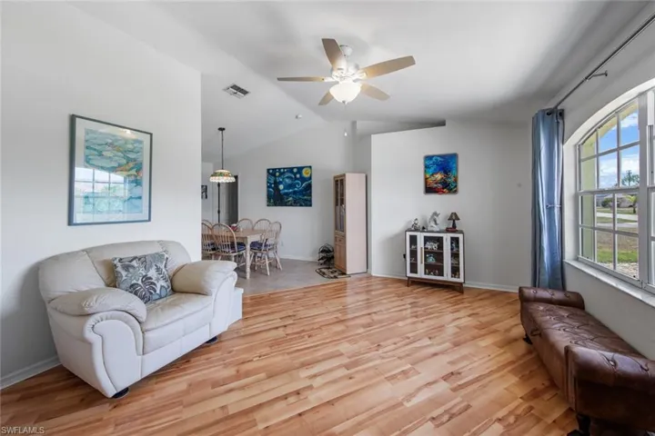 Living room with lofted ceiling, light wood-style floors, ceiling fan, and baseboards