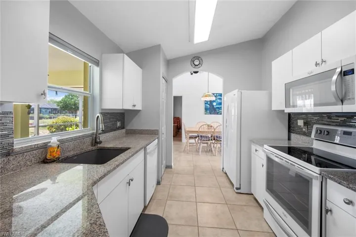 Kitchen with white appliances, a sink, tasteful backsplash, white cabinets, and light stone countertops