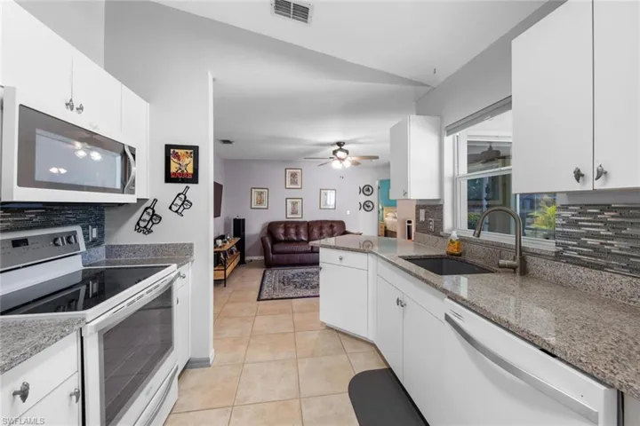 Kitchen featuring white appliances, a sink, backsplash, and vaulted ceiling