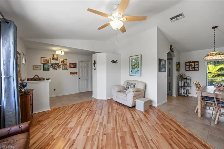 Living area with lofted ceiling, arched walkways, ceiling fan, light wood-style flooring, and baseboards