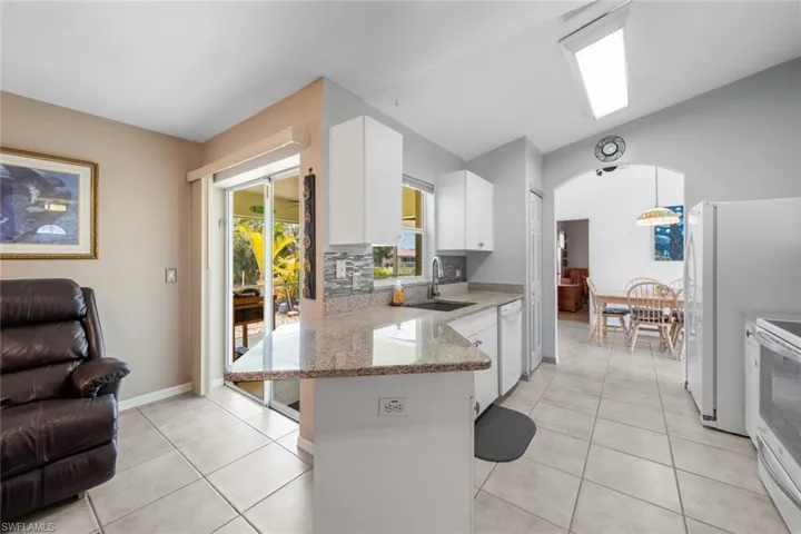 Kitchen featuring a sink, white appliances, white cabinets, a peninsula, and light stone countertops
