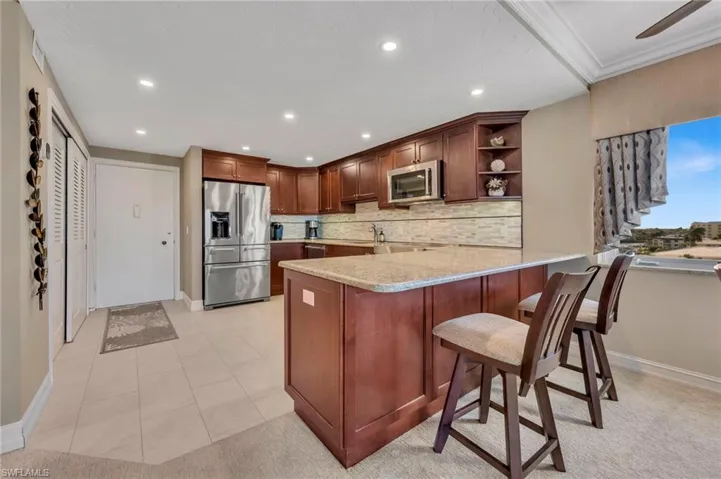 Kitchen featuring open shelves, a peninsula, stainless steel appliances, light stone countertops, and a breakfast bar