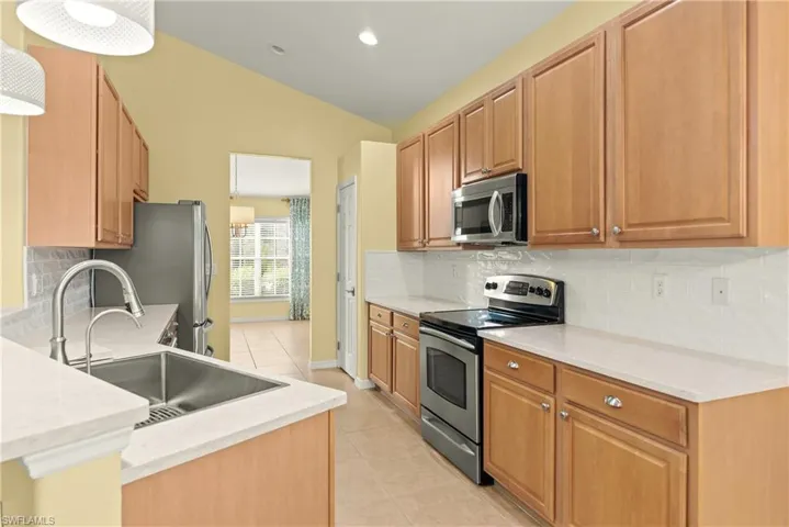 Kitchen featuring decorative backsplash, appliances with stainless steel finishes, light stone counters, and lofted ceiling
