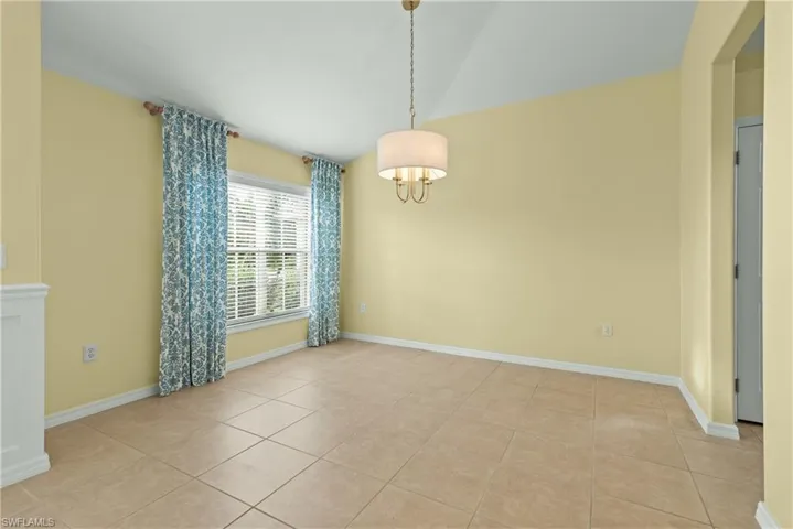 Empty room with light tile patterned floors, a chandelier, and lofted ceiling