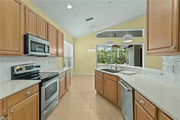 Kitchen featuring backsplash, appliances with stainless steel finishes, light stone countertops, hanging light fixtures, and a peninsula