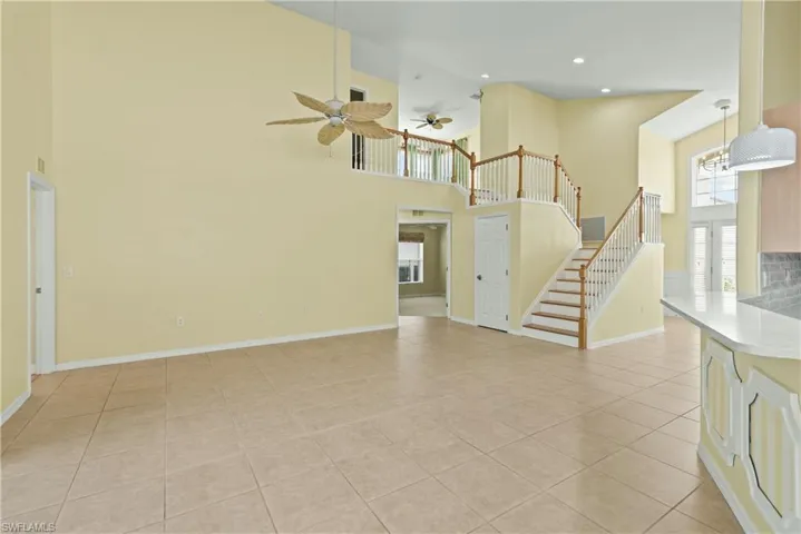 Unfurnished living room with a high ceiling, stairway, light tile patterned floors, recessed lighting, and ceiling fan