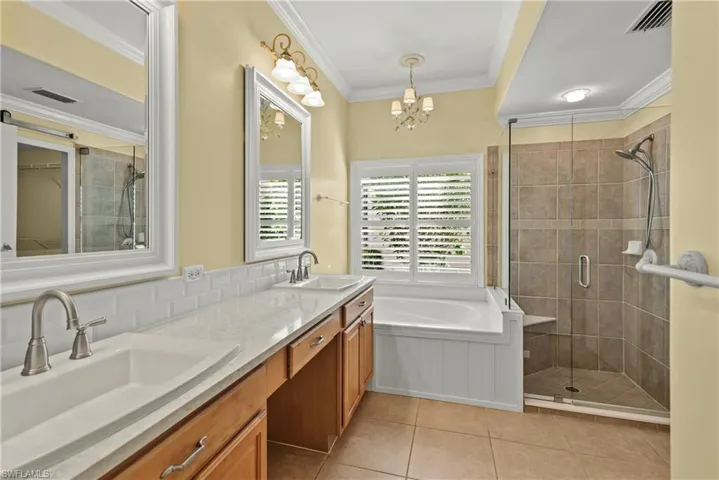 Master bath with crown molding, a shower stall, a garden tub, light tile patterned flooring, and double vanity