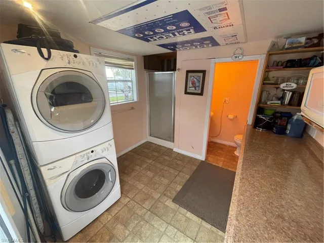Washroom with stacked washer and clothes dryer and baseboards