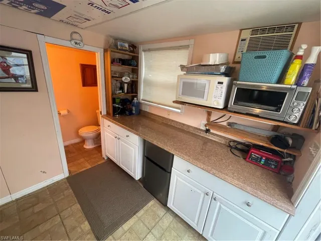 Kitchen with white cabinetry, open shelves, fridge, stone finish flooring, and an AC wall unit