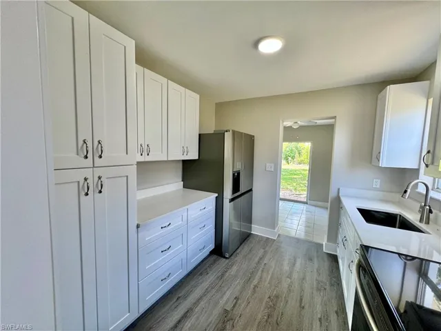 Kitchen featuring white cabinetry, black range with electric stovetop, dark wood-style floors, stainless steel fridge, and light stone counters