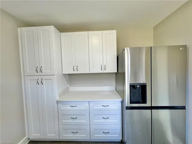 Kitchen with stainless steel fridge with ice dispenser, white cabinets, and light stone countertops