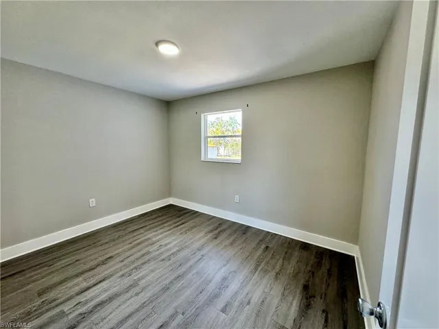 Unfurnished room with baseboards and dark wood-style floors